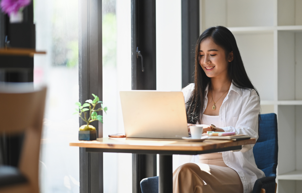 Woman working on a laptop at a cafe table by a window.