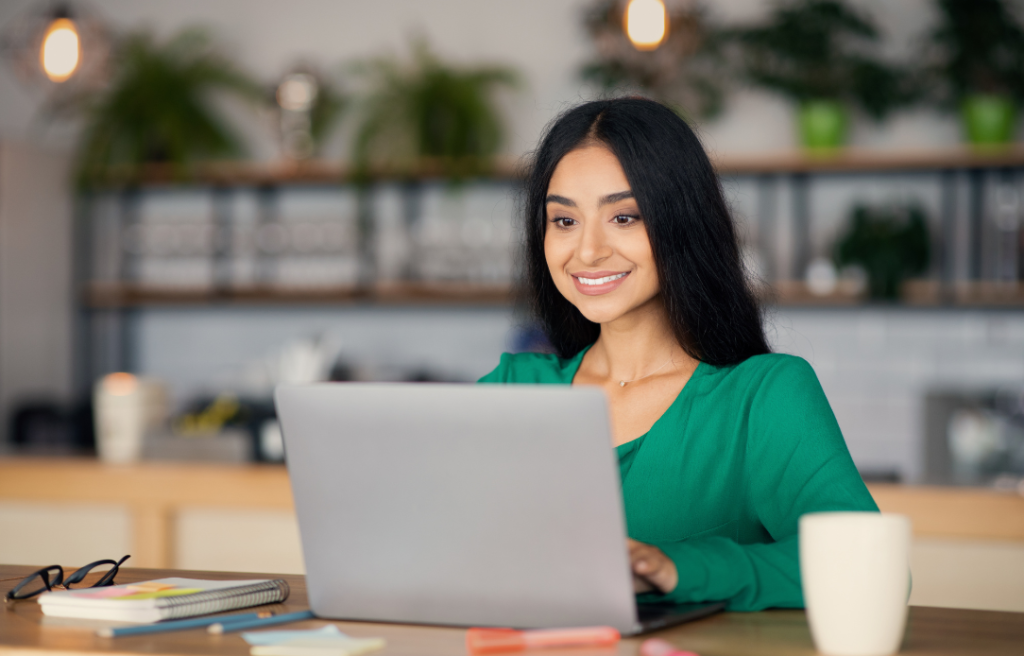 Smiling woman in a green top working on a laptop at a cafe.
