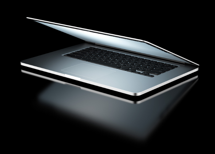 Opened silver laptop with black keyboard, reflected on a dark surface.